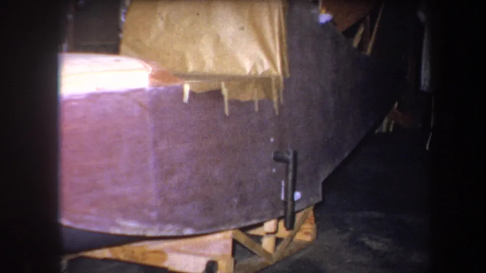 Final 1964 home-movie frame of the wooden boat hull, support cradle, and workshop materials in Yucaipa.