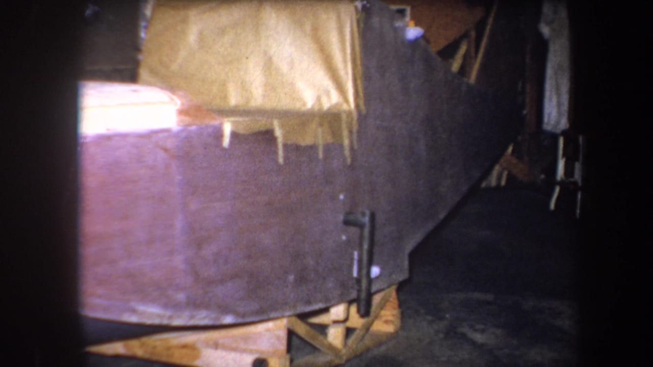 Tarp-covered wooden structure on blocks in a dark interior space.