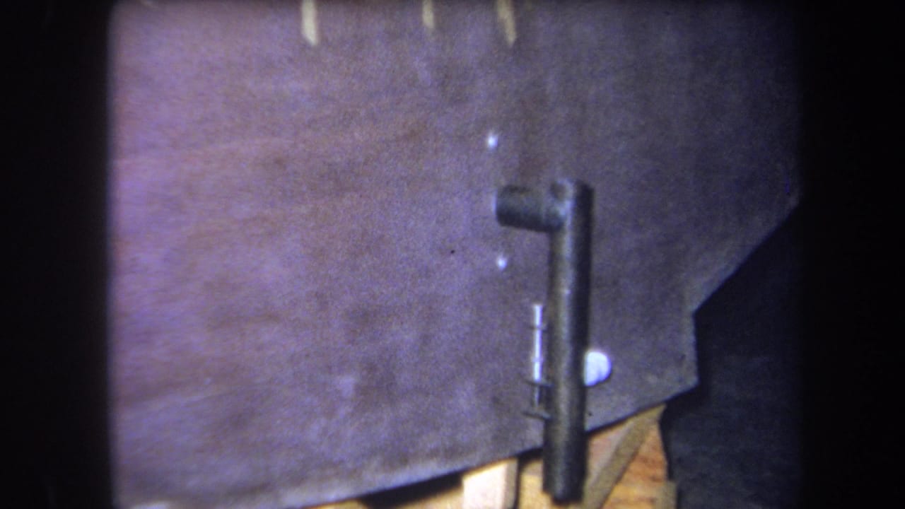1964 Volmer Yucaipa 8mm frame showing painted wood, support blocks, and an attached black metal bracket in close view.