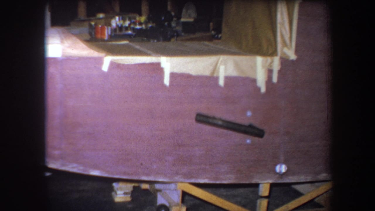 Dark cylindrical object on a wooden tabletop with fabric and furniture visible beyond the frame.