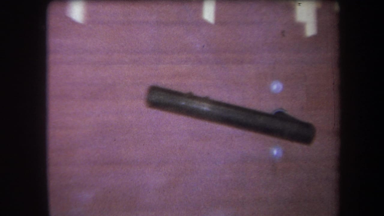 Closer view of a dark cylindrical object lying diagonally on a wooden surface.
