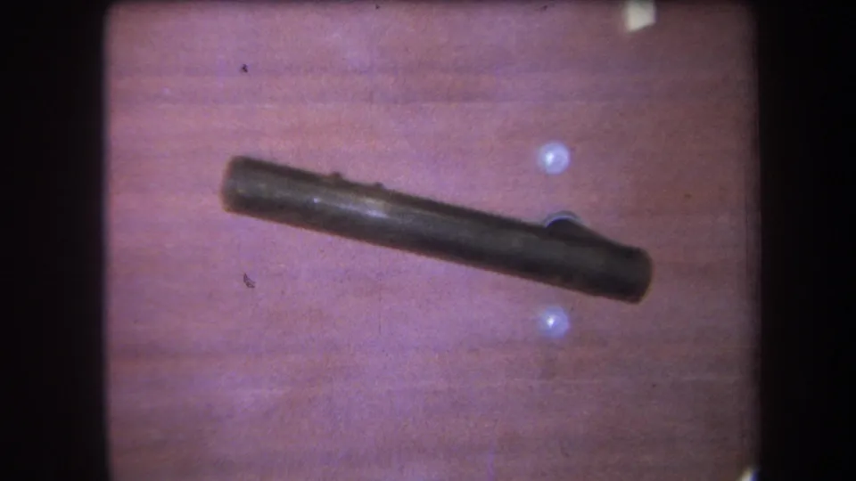 Tight 8mm close-up from 1964 showing the dark object and a raised side detail against a warm wood surface.