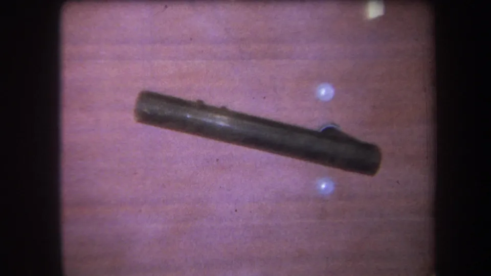 1964 Yucaipa home-movie frame showing a dark metal rod or handle against wood paneling with small pale wall holes.