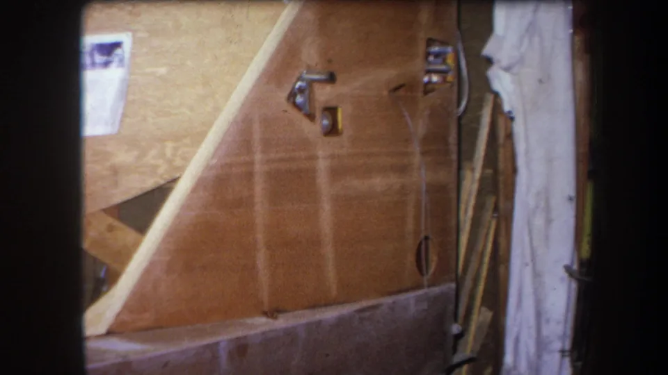 1964 Yucaipa interior renovation view showing wood wall panels, metal fixtures, wall holes, a hanging cloth, and stacked materials.