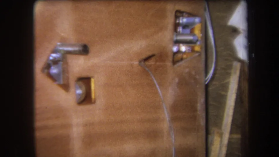 Tight 1964 Yucaipa home-movie frame of wood grain, a metal bracket, a small opening, and a thin wire crossing the panel.