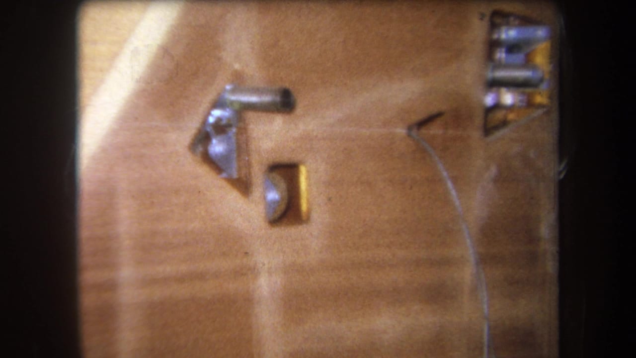 1964 8mm close-up from Yucaipa-area footage showing metal components mounted in a wooden surface with a thin wire crossing the frame.