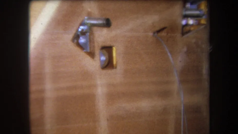 Close 1964 8mm frame of a wooden surface with a silver fitting, brass-colored piece, small round element, and curved wire.