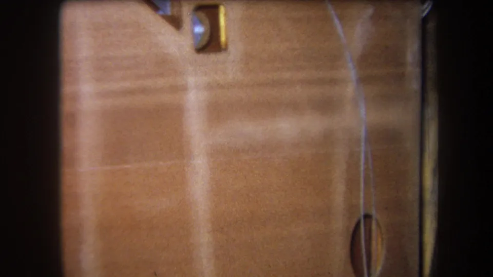 1964 8mm detail of the lower wooden surface, showing a thin vertical wire and round inset element near the right edge.