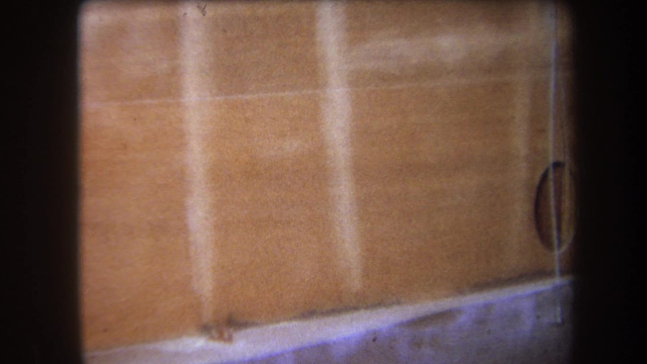 1964 Yucaipa home-movie frame showing a close-up of wood panels, grain, seam lines, and a partial circular opening.