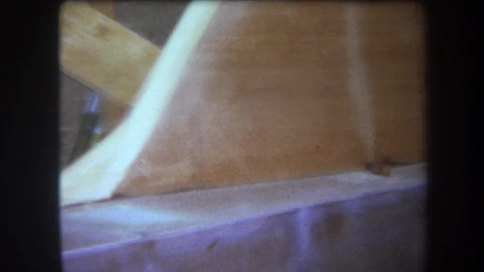 Close 1964 Yucaipa home-movie view of a pale curved strip over brown wood grain, seams, and a lower wooden ledge.