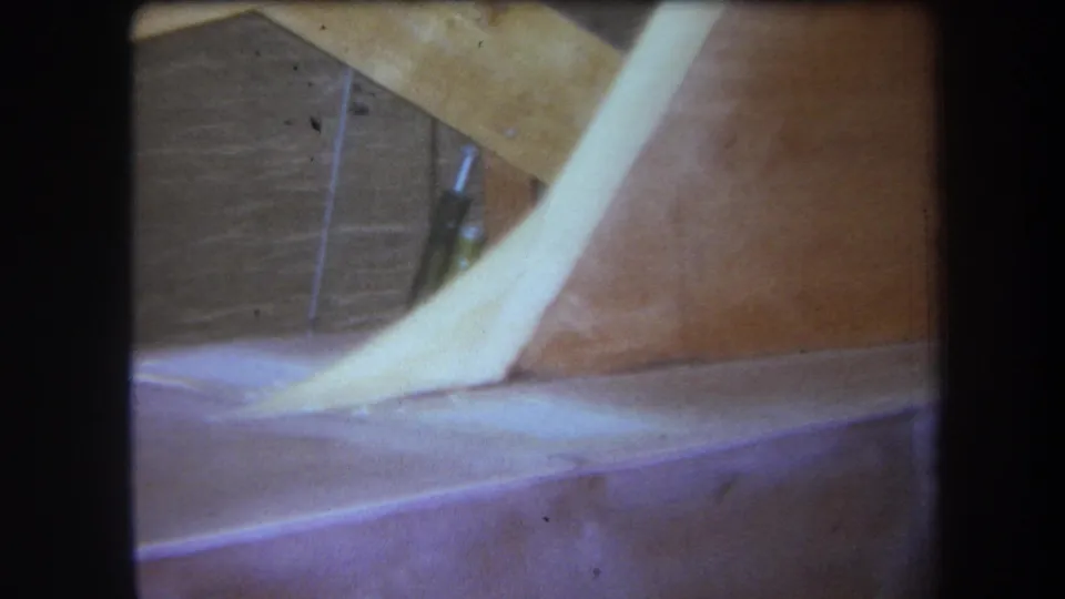 1964 Yucaipa frame showing a pale curved strip against brown wood, with seams, grain, and a darker rectangular area visible behind.