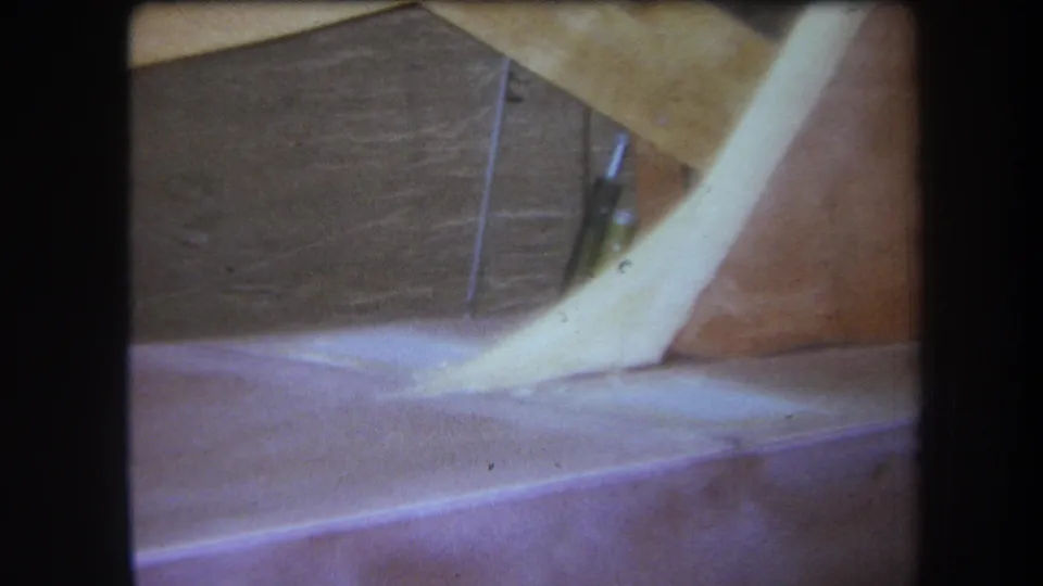 1964 8mm frame from the Yucaipa-area reel showing a dim attic corner with exposed wood, a pale angled form, and soft faded color.