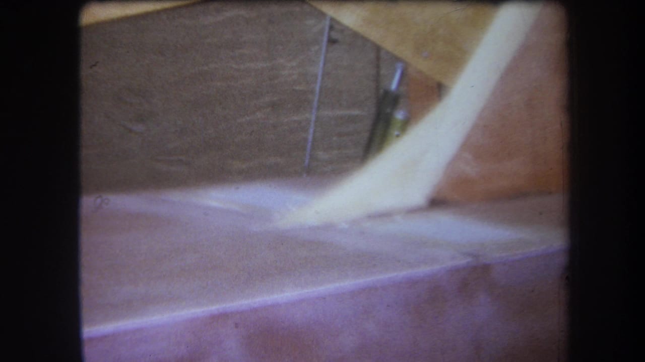 1964 Yucaipa-area home-movie frame showing an unfinished attic detail with wood planes, a pale sloping form, and low-light grain.