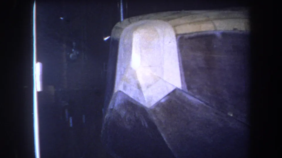 1964 8mm frame from the Yucaipa-area reel showing a dark attic space, rough wood, and a pale draped or insulation-like shape.