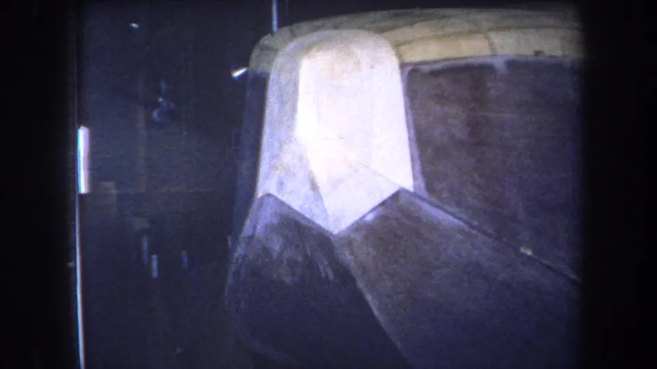 1964 Yucaipa-area 8mm frame showing a pale curved bow-like surface against a dark worn hull in dim interior light.