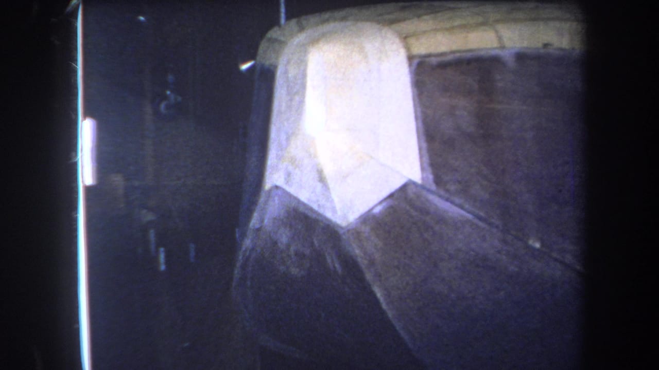 1964 8mm frame from Yucaipa showing the same worn boat-like hull surface, held close in a dark indoor setting.
