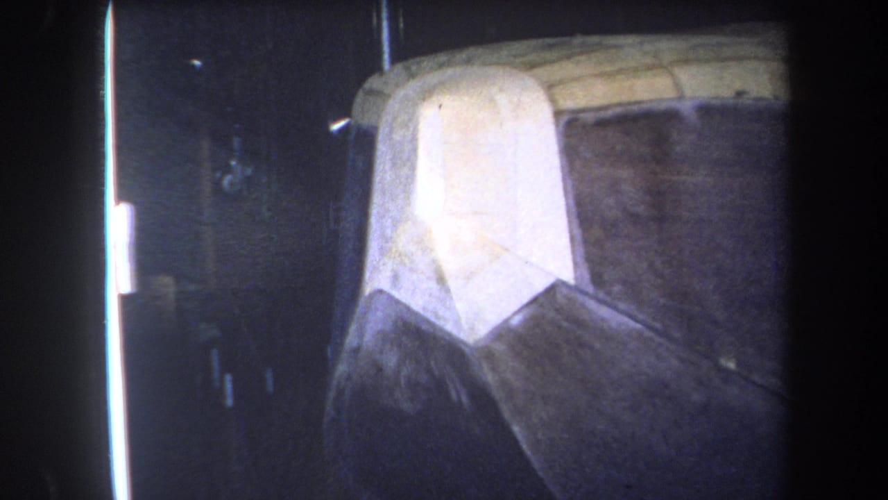 1964 Yucaipa-area 8mm frame showing a close-up of a wooden aircraft nose and fuselage repair or build section in dim indoor light.