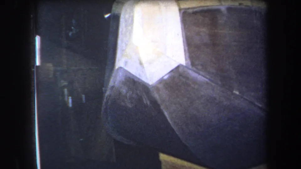 1964 Yucaipa 8mm frame showing the sculpture from close range, with soft focus on white, black, brown, and yellow painted surfaces.