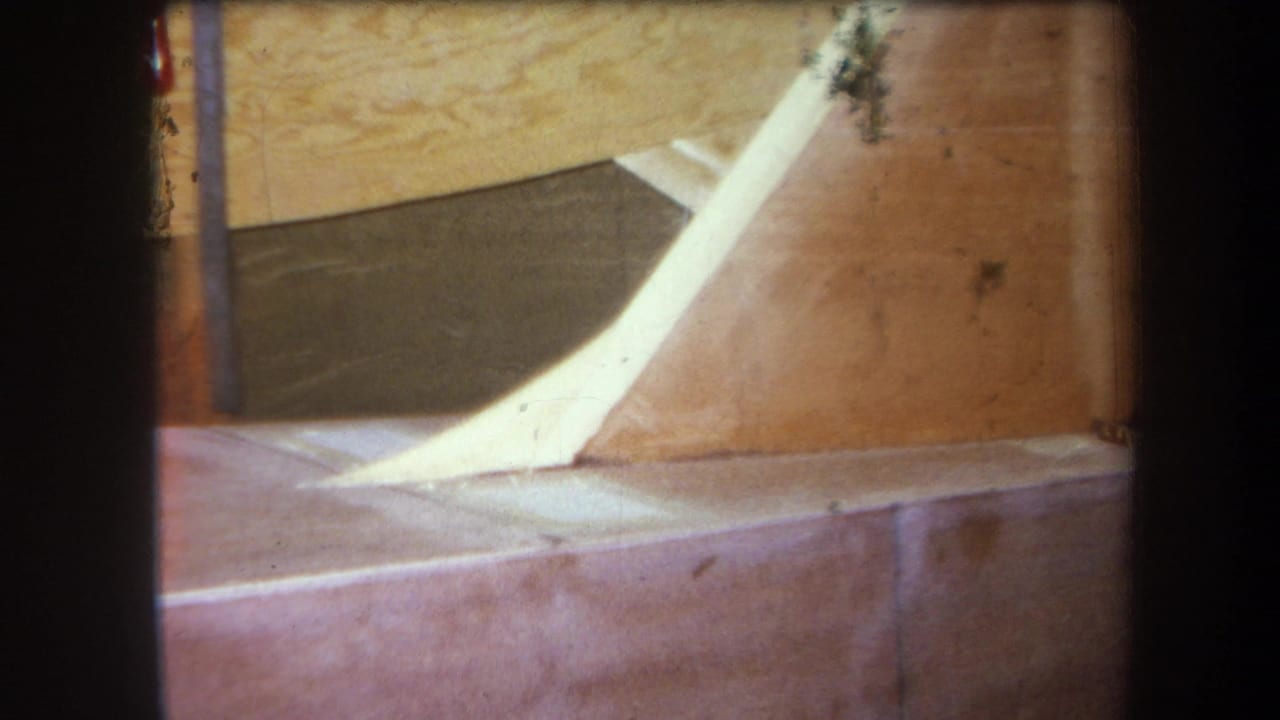 1964 Yucaipa-area 8mm frame showing a wooden structure, pale angled ramp or chute, and reddish platform surface.