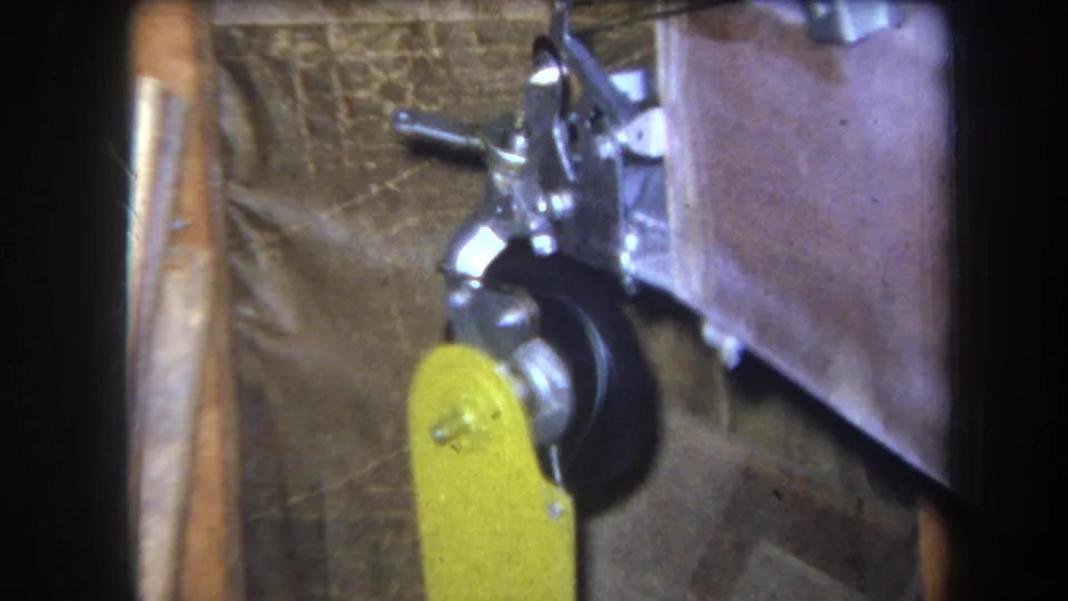 Final 8mm frame of the Yucaipa-area mechanical detail, showing the yellow lever and black wheel under a compact metal linkage.
