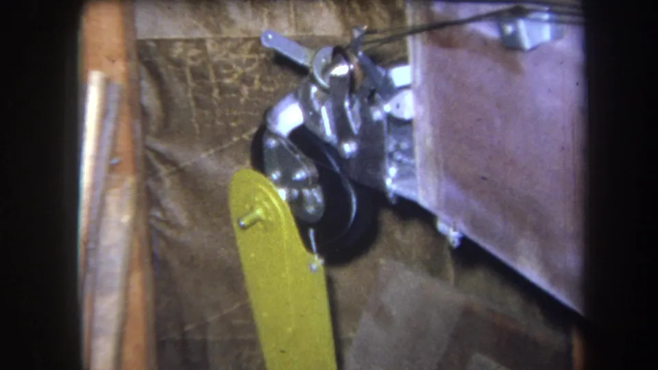 Close 8mm view of a yellow paddle-like part near a black wheel and metal bracketry, supported by the clip's 1964 Yucaipa metadata.