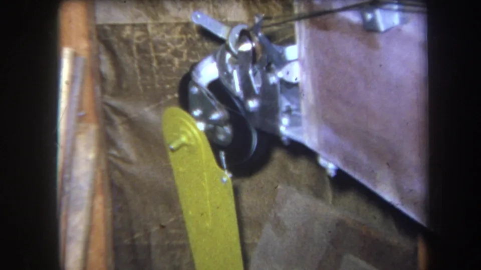 Handheld 8mm frame of a small pulley system with metal hardware, a black wheel, and yellow paddle attachment in a dim interior.