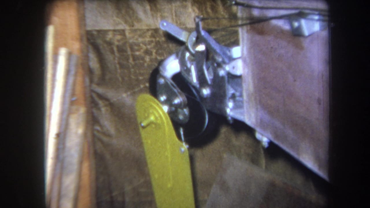 1964 Yucaipa 8mm frame showing a yellow lever, black wheel, and shiny metal linkage on a small mounted mechanical device.