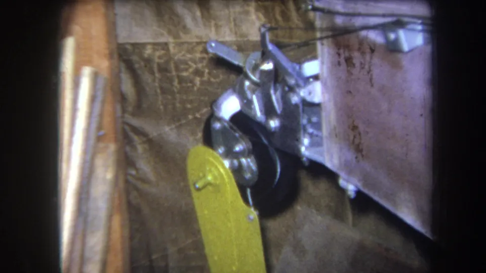 1964 Yucaipa 8mm frame with the yellow lever near the black wheel and metal mechanical assembly on a wooden structure.