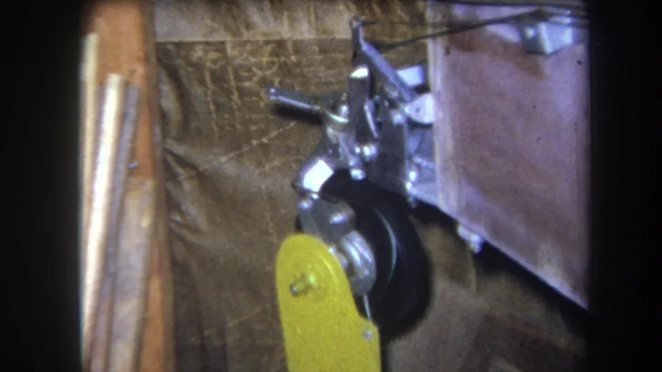 1964 Yucaipa 8mm frame showing the yellow lever low against a black wheel, metal linkage, wood support, and brown backing.