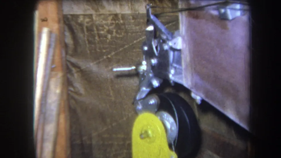 1964 Yucaipa 8mm frame showing the same mechanical part from a slightly shifted handheld angle, with lever, wheel, and metal mount.