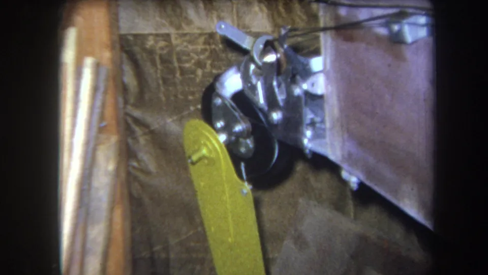 1964 Volmer, Yucaipa 8mm frame showing the yellow lever angled across a black wheel and metal joint near wood and fabric-like materials.