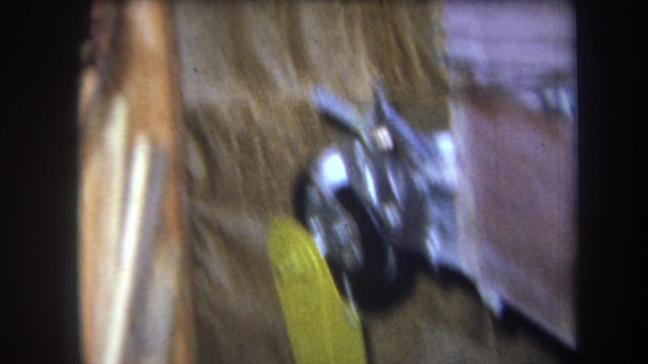 1964 8mm frame from Volmer Yucaipa showing a soft, close view of yellow-painted metal hardware near an aged wall surface.