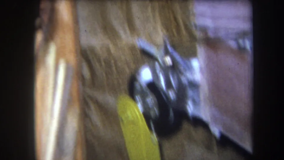 1964 8mm frame from Volmer Yucaipa showing a soft, close view of yellow-painted metal hardware near an aged wall surface.