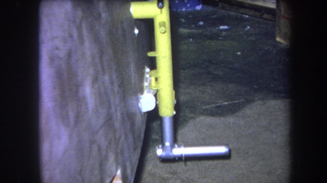 Yellow vertical pipe assembly with a silver T-shaped handle against a wall.