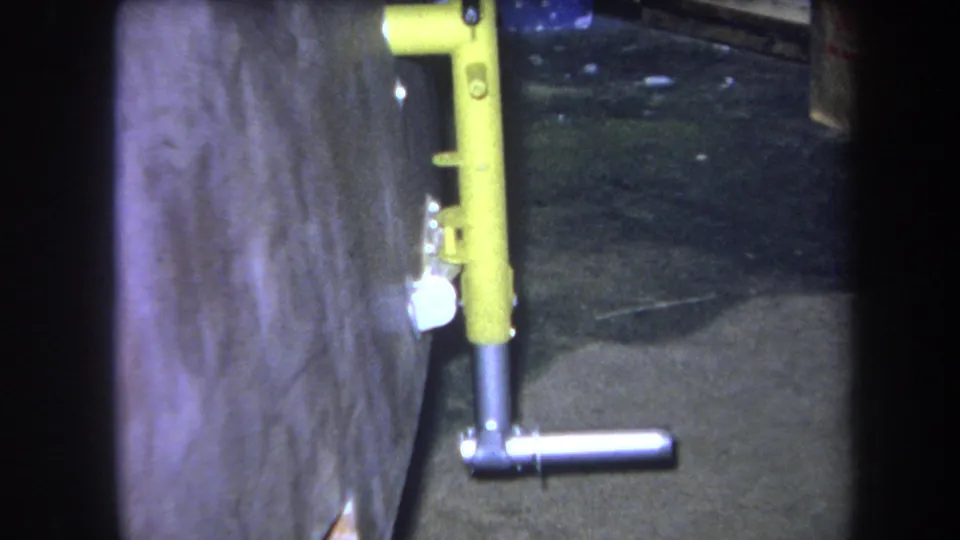 1964 Volmer Yucaipa frame showing a yellow vertical pipe or valve assembly with a silver horizontal handle beside a weathered wall.