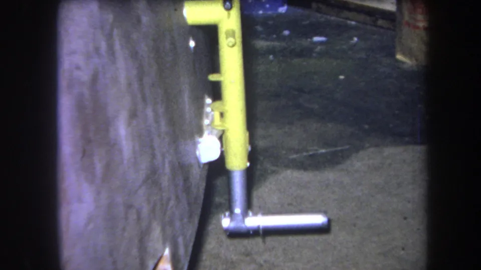 1964 8mm frame in Volmer Yucaipa showing the yellow metal assembly, silver handle and wall surface from a steady close angle.