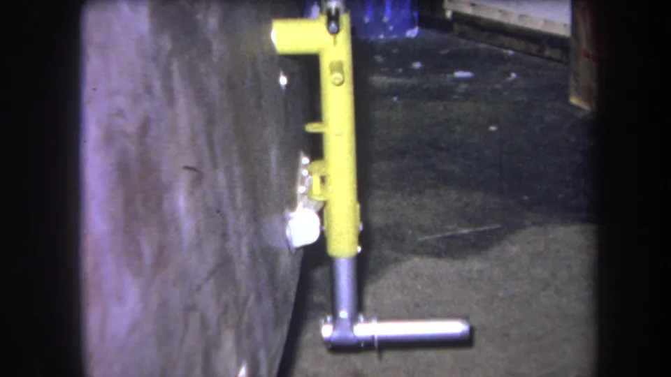 1964 Volmer Yucaipa 8mm frame showing the yellow and silver fixture slightly lower in frame, with concrete wall and floor detail.
