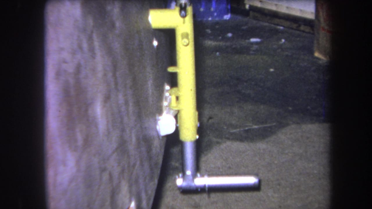 Yellow metal coupling beside a wall with a silver horizontal handle near the floor.