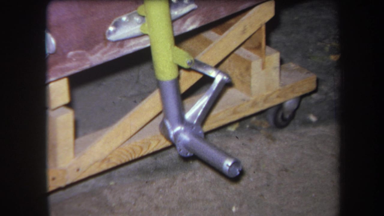 1964 Yucaipa home-movie frame showing the same yellow handle and polished metal assembly beside rough wood supports and a caster wheel.