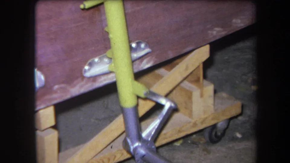 1964 Yucaipa frame with the yellow handle crossing a red-brown panel above a silver arm and wooden caster-mounted support.