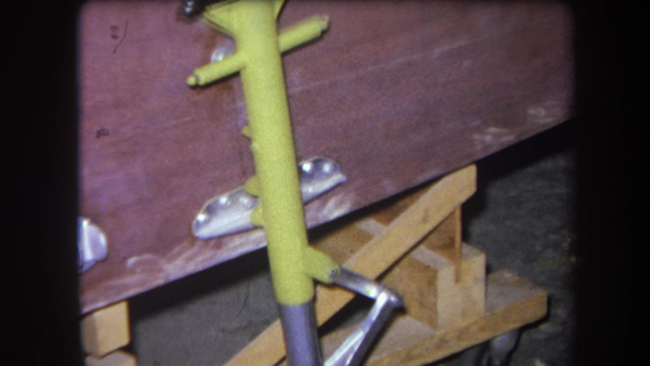 Yellow metal fixture leaning against a reddish wooden surface with silver brackets and wood supports below.