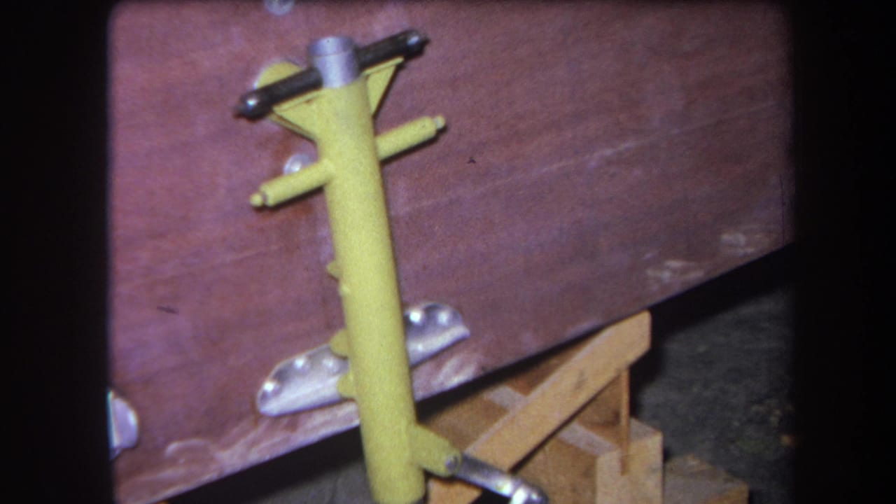 Close 8mm view of a yellow-painted metal fixture mounted or resting near a worn wooden bench in Yucaipa, 1964.