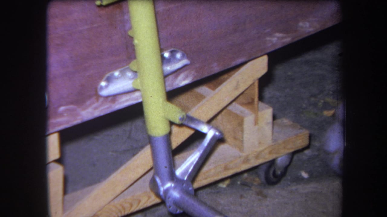 Close 8mm view of the handmade transport cart's underside, showing wood supports, metal hardware, and a wheel.