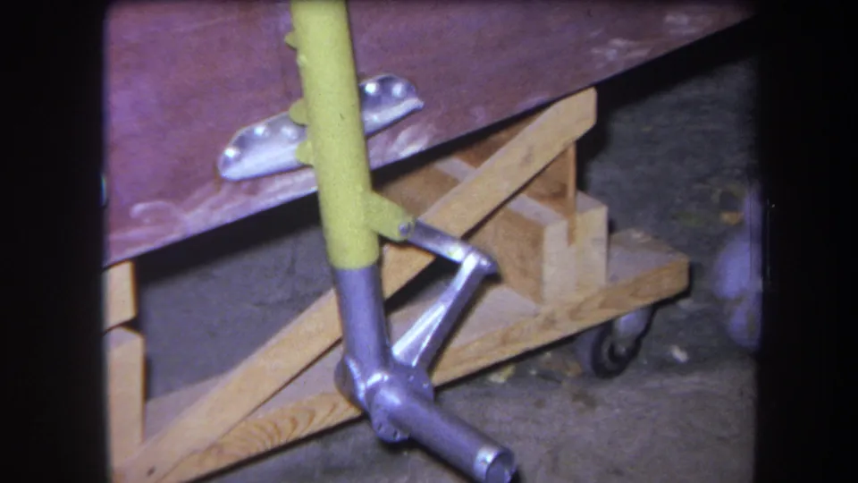 1964 home-movie still of the cart's lower frame, with yellow metal tubing attached to a wheeled wooden base.