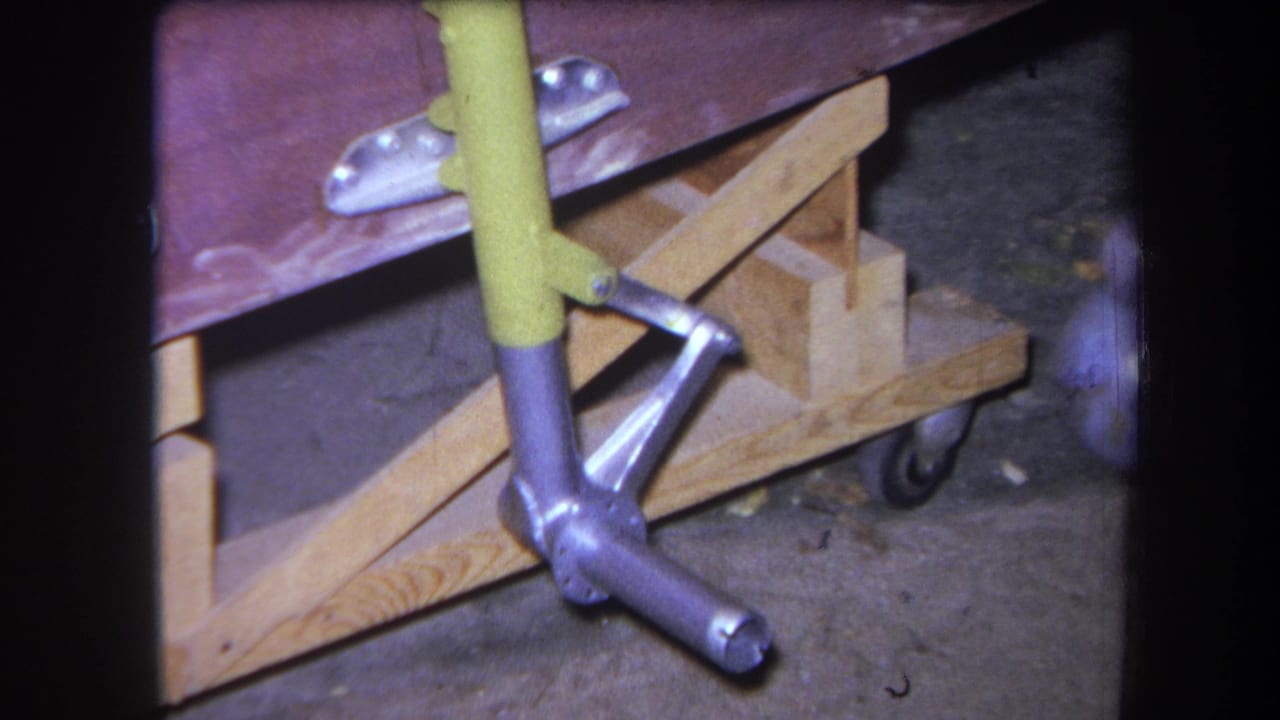 Close view of a yellow-handled tool beside a wooden support and metal vehicle component.