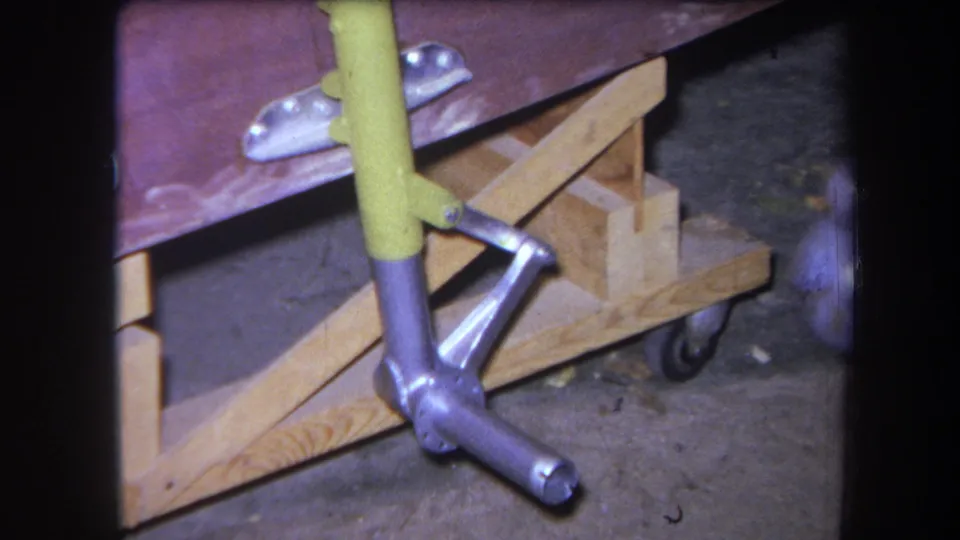 1964 8mm frame from Yucaipa showing a yellow-handled tool near wood bracing and a stripped vehicle construction detail.