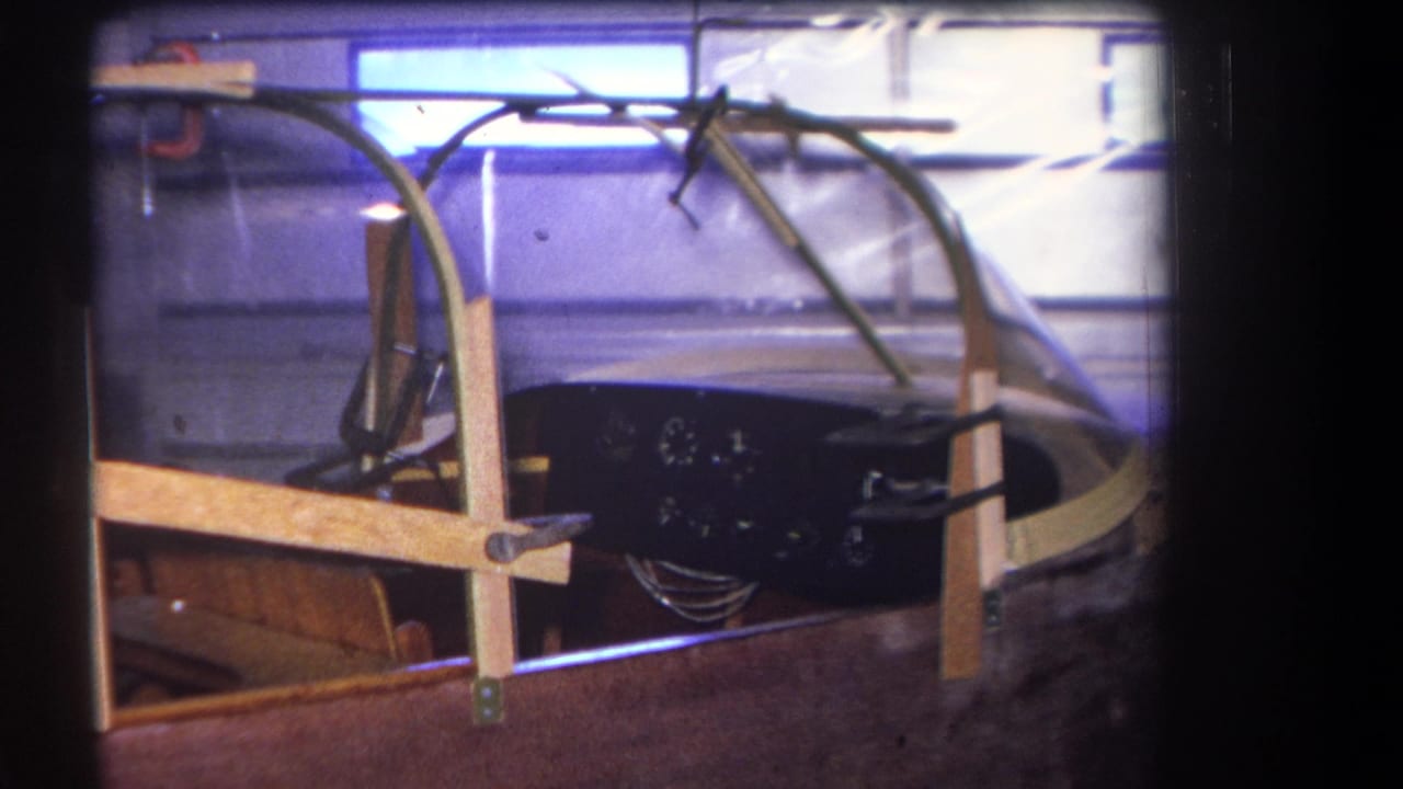 Partly built aircraft cockpit with clear canopy, wooden braces, clamps, and dark instrument panel.