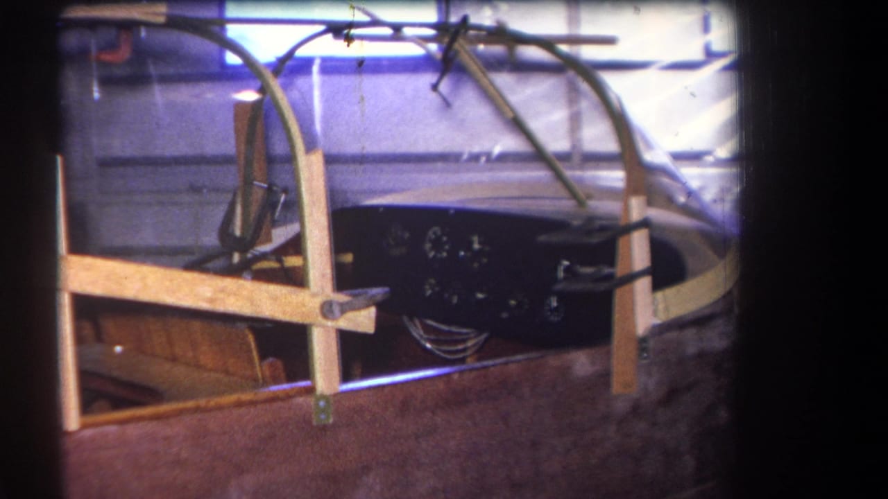 Aircraft cockpit section with clear canopy, wood brace, dark dashboard and visible gauges.