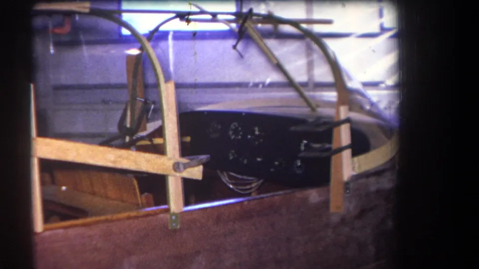 1964 Yucaipa-area footage frame of an idle aircraft cockpit section, showing canopy glass, wood bracing and analog instruments.
