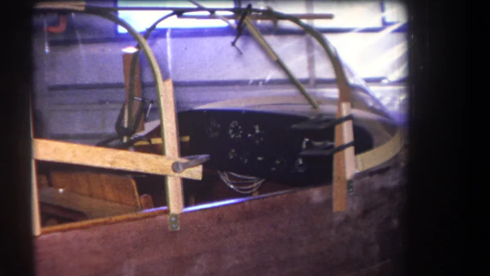Close 8mm frame from 1964 showing a stored aircraft cockpit in Yucaipa, with wood framing, canopy material and a dark gauge panel.